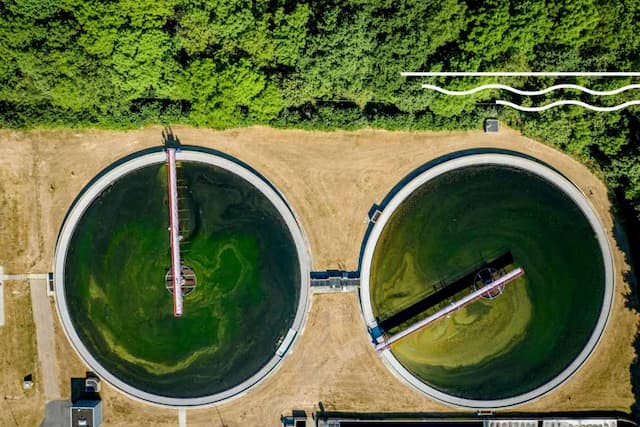 Aerial view of two circular wastewater treatment clarifiers with green water and rotating arms at a water treatment plant